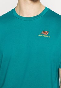 Tyrkysové bavlněné tričko s kulatým výstřihem a krátkými rukávy, s vyšívaným vícebarevným logem "New Balance" na hrudi.
