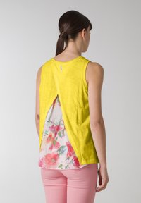 Gul ärmlös topp med en slits bak, som avslöjar ett foder med blommönster i rosa, grönt och vitt. Lättviktig tyg.