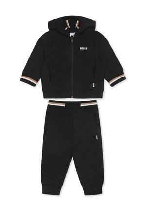 Ensemble en deux pièces noir comprenant un sweat à capuche zippé et un pantalon assorti. Les détails incluent des rayures sur les poignets et la ceinture.
