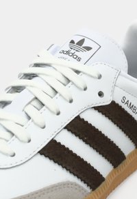 Adidas Samba shoes with a white leather upper, brown suede stripes, textured tan rubber sole, and flat white laces.