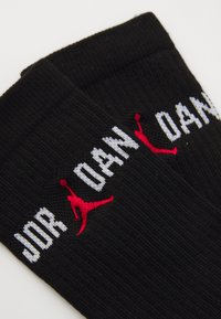 Calcetines negros acanalados con el texto blanco "JORDAN" y un logo de Jumpman rojo bordado cerca del puño superior.