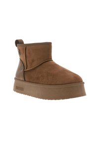 Brūni zamšaini zābaki līdz potītei ar noapaļotu purngalu, zemu potītes augstumu un biezu gumijas platformas zoli. Iekļauj sānu logotipu un šuvju detaļas.