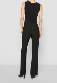 Haut sans manches noir associé à un pantalon taille haute noir, affichant une texture lisse et une coupe droite. Talons aiguilles noirs visibles.
