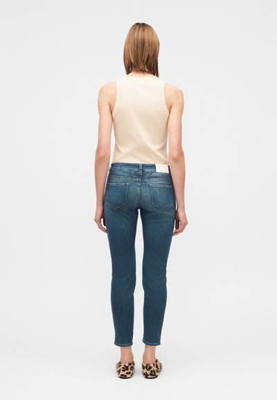 Canottiera beige chiaro, jeans skinny blu con due tasche posteriori e scarpe slip-on con stampa leopardata. Tessuto liscio e vestibilità classica.