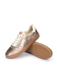 Zapatillas metálicas de bronce con acentos blancos, suela de goma texturizada y diseño con cordones. Presenta un logotipo en el costado y la lengüeta.