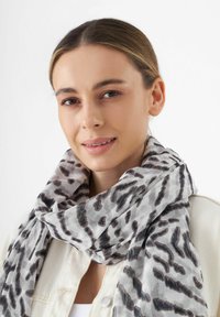 Écharpe légère en imprimé léopard dans des tons de gris et de noir, avec une texture fluide enroulée autour du cou.