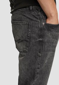 Schwarze Jeans aus Denim mit einer verblassten Textur, Fünf-Taschen-Design und einem markanten Stichdetail auf der Hintertasche.