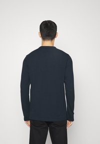 Marineblaues Langarmshirt aus weichem Baumwollmaterial. Verfügt über einen Rundhalsausschnitt und einen lockeren Schnitt, ohne sichtbare Logos oder Muster. Einfaches und minimalistisches Design.