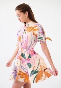 Abito a maniche corte con design floreale nei toni pesca e colori vivaci. Presenta una chiusura con bottoni sul davanti e una gonna svasata con maniche legate.