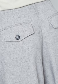 Lys grå bukser lavet af tekstureret stof med subtilt mønster, der har to baglommer med knaplukninger.