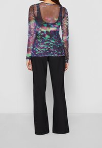 Transparante top met lange mouwen en een kleurrijk abstract patroon in paars en groen, gecombineerd met zwarte, hooggetailleerde, wijde broekspijpen.