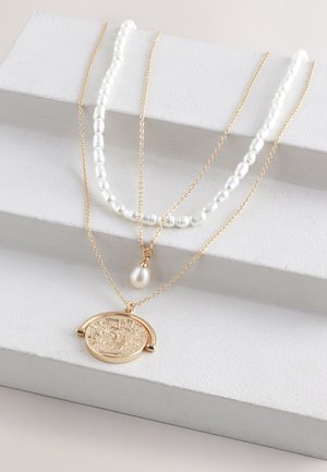 Goldfarbenes, mehrschichtiges Halskettenset mit strukturiertem Anhänger, ergänzt durch weiße Perlen- und Perlenketten. Die Ketten variieren in Länge und Dicke.