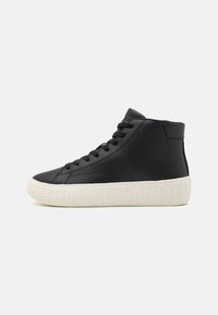 Svart hög-top sneakers med svarta snören och vit sula präglad med "TOMMY JEANS"-logotyp på en enfärgad bakgrund.