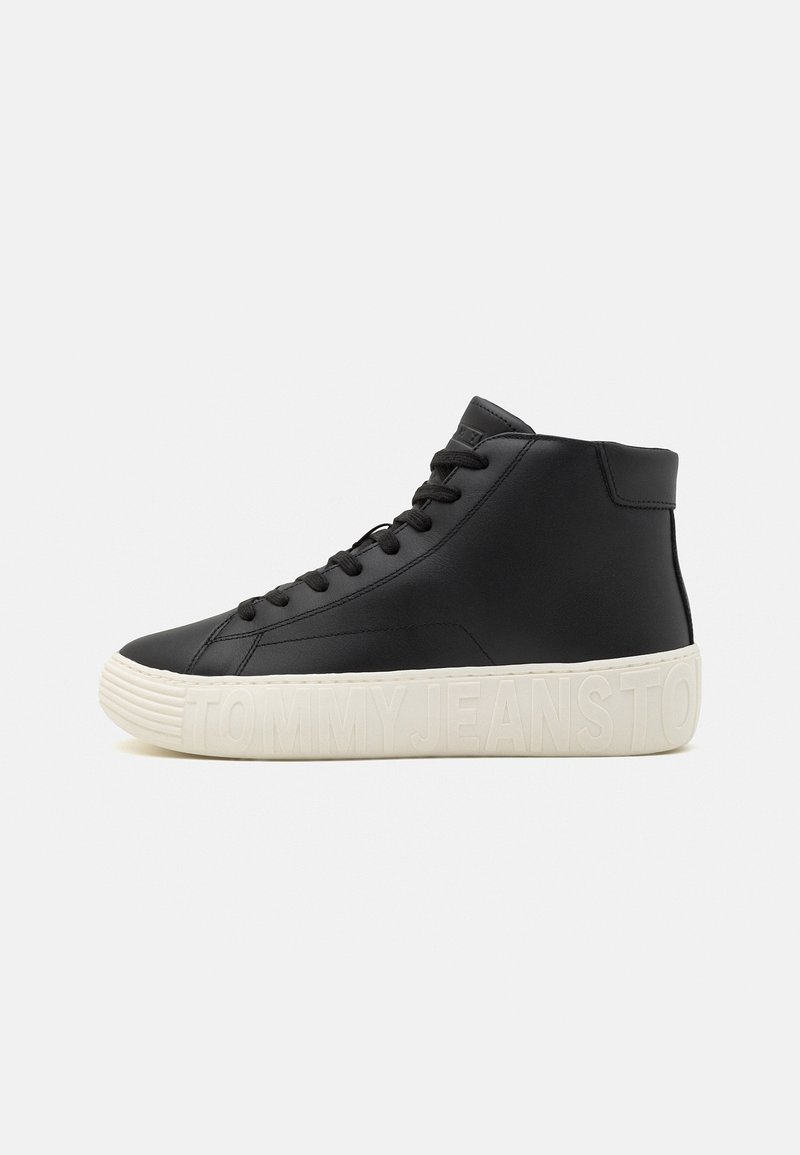 Svart hög-top sneakers med svarta snören och vit sula präglad med "TOMMY JEANS"-logotyp på en enfärgad bakgrund.