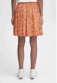 Oranje luipaardprint rok met een geplooide tailleband en een knie-lengte ontwerp. Draag het met witte hoge sneakers. Soepele, lichte stof.