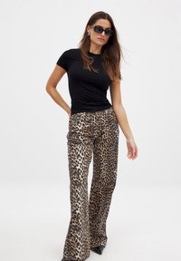 Camiseta negra ajustada combinada con pantalones de leopardo de tiro alto y acampanados, con una textura suave y un audaz patrón en negro y marrón.