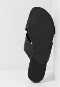 Sandale noire avec semelle texturée et brides croisées, taille 37, présentée sur un fond blanc en angle.