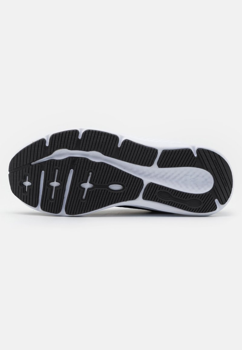 La suela de una zapatilla deportiva en blanco y negro presenta un patrón de goma segmentado con surcos para mejorar la adherencia y la flexibilidad. Material liso y texturizado.