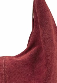 Sac en daim bordeaux au toucher doux, de forme incurvée, avec des coutures visibles et une fermeture éclair en métal en accent sur le bord.