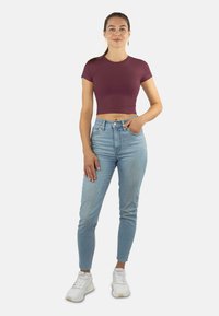 Burgunderfarbenes Crop-Top, enganliegendes Design mit kurzen Ärmeln, kombiniert mit hoch taillierten hellblauen Skinny Jeans und weißen SportSneakern.