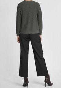 Sweter w oliwkowej zieleni z teksturowanym wzorem bobble, z okrągłym dekoltem, długimi rękawami, zestawiony z czarnymi szerokimi spodniami i dopasowanymi botkami na obcasie.