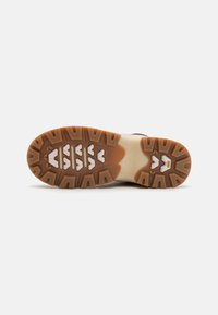La semelle de chaussure est dotée d'une accroche en caoutchouc avec un profil de semelle multi-patron en marron et blanc. Les bords courbés améliorent la flexibilité et la traction.