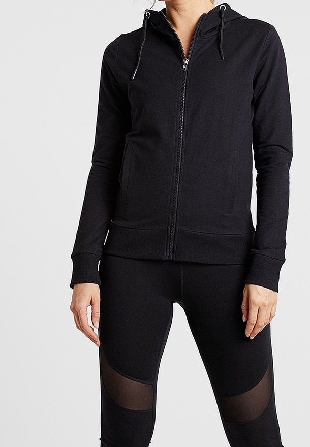 Sudadera negra con cremallera y capucha con cordón, fabricada en un tejido texturizado, con bolsillos laterales y puños acanalados, combinada con leggings negros a juego que cuentan con paneles de malla.