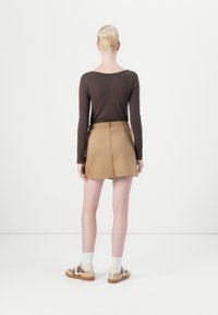 Braunes Langarmshirt, hellbrauter Kunstlederskirt mit geradem Schnitt und Sneakers im Tiermuster. Weiße Socken sind oberhalb der Schuhe sichtbar.