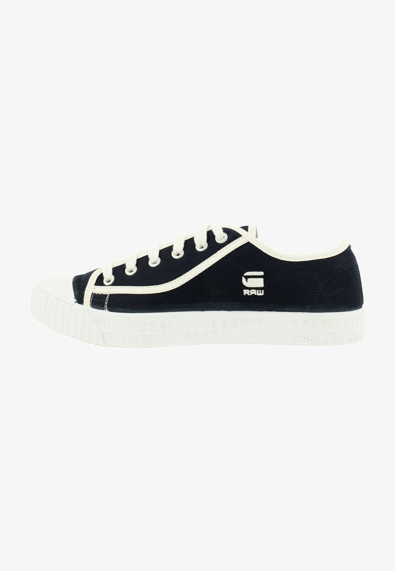 Marineblaue Canvas-Sneaker mit weißer Gummikappe und Sohle. Merkmale sind ein weißes Logo an der Seite und sechs Ösen für Schnürsenkel. Strukturierte Sohle.