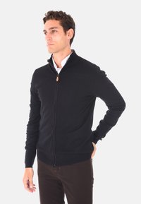 Felpa nera con zip e colletto alto, realizzata in tessuto a maglia, con una zip in pelle marrone e polsini e orlo a costine.