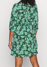Vestido floral con un fondo negro y grandes flores en tonos aqua y verde, mangas largas, cintura elástica y una apertura en forma de llave en la parte posterior.