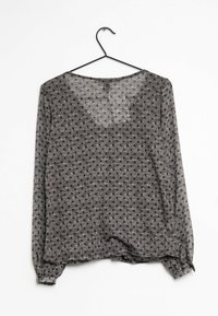 Blusa larga de mangas largas en negro y gris con un patrón de lunares, que presenta un cuello redondo y puños elásticos. Cuela de un gancho negro.