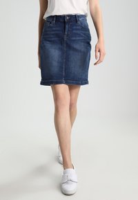 Džínová sukně v tmavě modré barvě, délky po kolena, s těsným střihem. Obsahuje zapínání na knoflík, poutka na opasek a lem s mírným třepením.