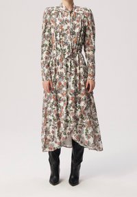 Lång klänning med blommönster i vitt med gröna, rosa och blå mönster. Har hög halsringning, långa ärmar och en samlad midja.