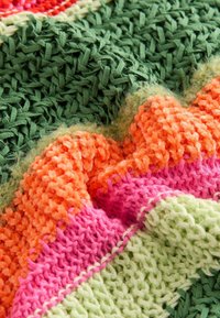 Flerfärgad vävd filt med gröna, orangea, rosa och ljusgröna sektioner, med varierande texturer och en scalloped design.