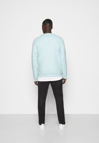 Ljusblå sweatshirt med raglanärmar, i kombination med svarta byxor med sidostriper och vita sneakers. Slät tyg, ledig passform.