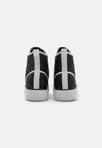 Černé vysoké tenisky s texturovanými materiály, bílými akcenty a vzorovaným designem na stranách. Silné bílé gumové podrážky.