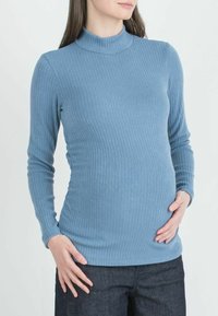 Maglietta a maniche lunghe in morbido tessuto blu a coste, caratterizzata da un collo alto e una forma aderente, indossata su pantaloni in denim scuro.