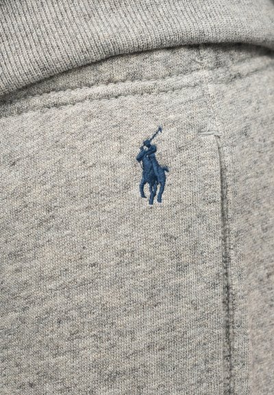 Γκρι πλεκτό ύφασμα με ένα μικρό κεντητό λογότυπο παίκτη πόλο σε σκούρο μπλε κοντά σε μια κάθετη ραφή ή άκρη τσέπης.