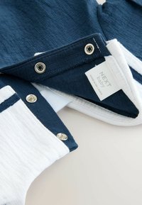 Marineblauw en witte babykleding met drukknoopjes, textuurstof en een label met de tekst "NEXT baby" en gemaakt in Sri Lanka.