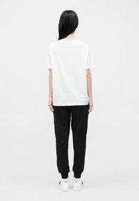 Biele tričko s krátkymi rukávmi, voľný strih, v kombinácii s čiernymi jogger nohavicami. Obe vyrobené z ľahkej látky. Biele tenisky s jemným logom.