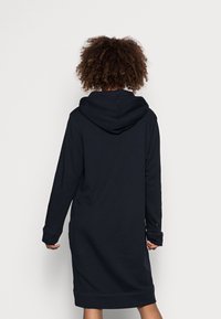 Marinblå klänning med huva gjord av mjukt material, med långa ärmar, sidofickor och ribbade ärmslut och fåll. Klassisk avslappnad design.