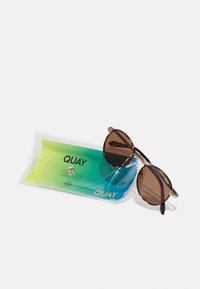 Ochelari de soare rotunzi din postav cu lentile maro, însoțiți de un pachet transparent care conține o cârpă din microfibră cu un gradient verde și albastru.