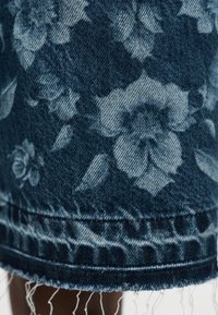 Τζιν ύφασμα με σκοτεινά και ανοιχτό μπλε λουλουδένια σχέδια και ξεφτισμένο τελείωμα στο κάτω άκρο ενός ενδύματος.