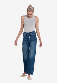 Hoogwaardige blauwe denim jeans met een rechte pijp en knoopsluiting. Gekleed met een lichtgrijze geribbelde tanktop en beige schoenen.