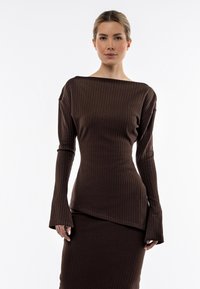 Top lungo a maniche lunghe marrone a coste con orlo asimmetrico. Presenta un ampio scollo e maniche svasate. Texture liscia, design aderente.