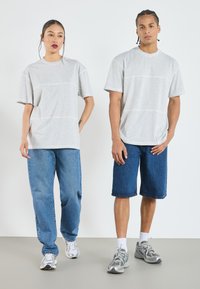 Grå kortermede T-skjorter i oversized passform, kombinert med blå denimjeans og shorts. Sneakers tilfører en sporty detalj til det uformelle antrekket.