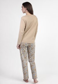 Blusa beige de manga larga con cuello redondo combinada con pantalones de pijama estampados que presentan acentos azules y diseños de dibujos animados sobre un fondo color tostado.