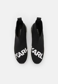 Černé pletené slip-on boty s vysokým vzorem, na každé straně s výrazným bílým logem "KARL" a texturovaným patníkem. Bílá gumová podrážka.