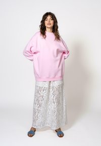 Per didelė rožinė pūkinė palaidinė, balta nėriniuota maksi sijonas su gėlių raštu ir mėlyni šlepetės. Lygus audinys, laisvas modelis ir banguoti rankogaliai.